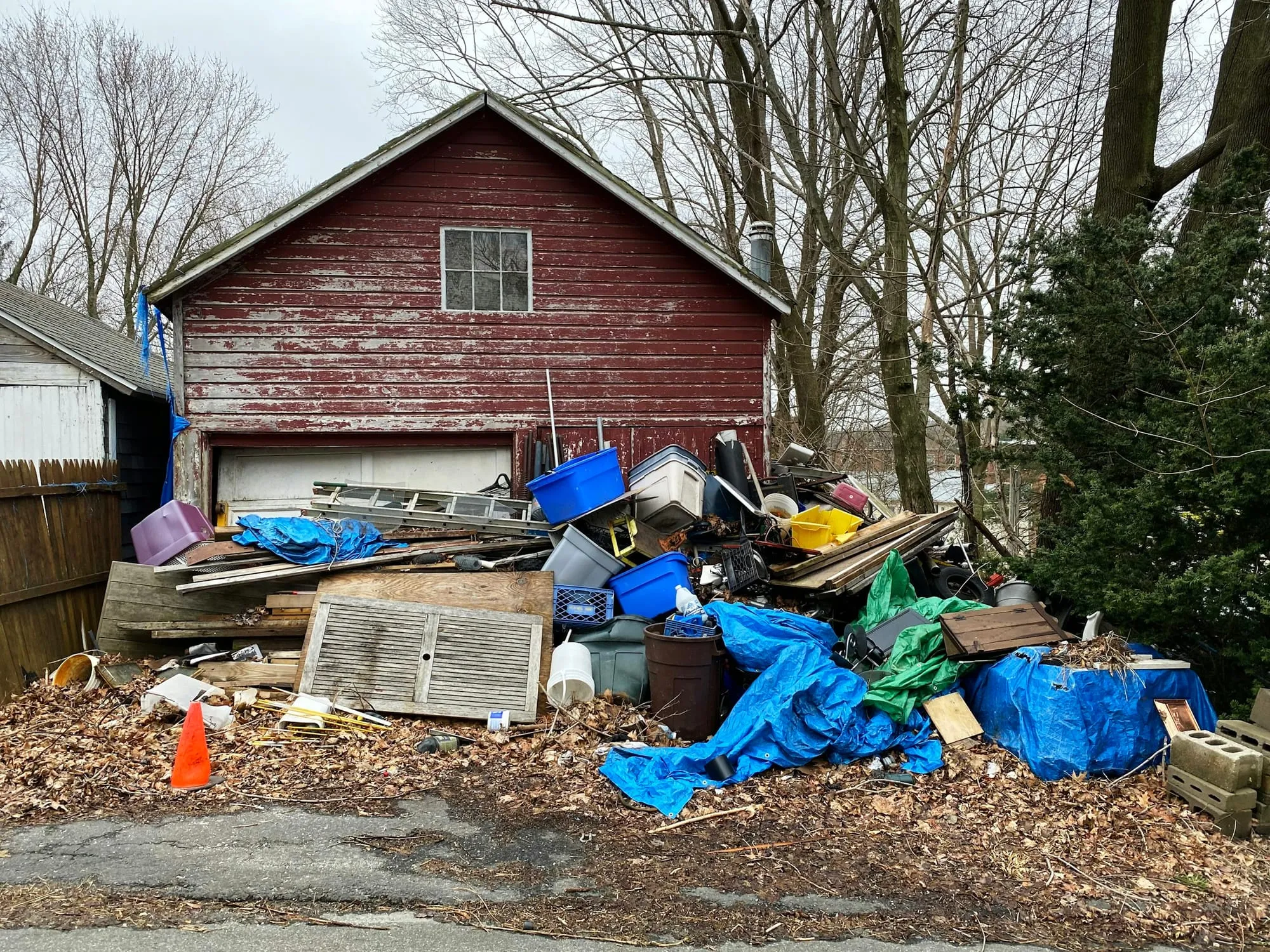 Pile of old junk, bins and tarps behind a weathered red barn